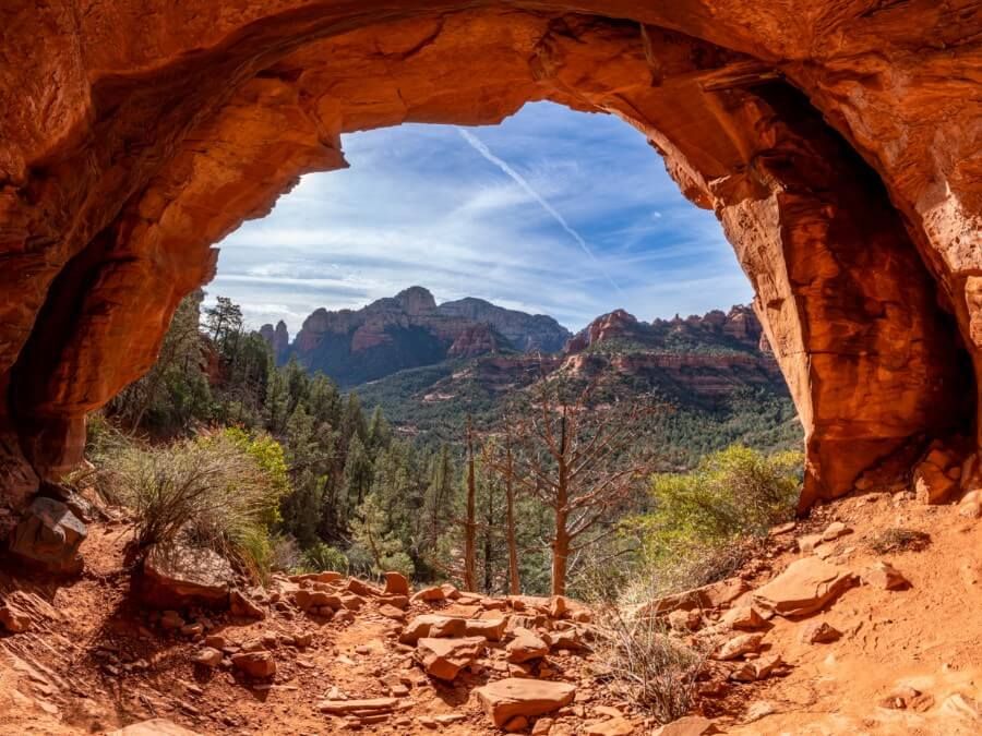 Enormous sandstone arch glowing orange under sunlight at the entrance to popular caves in Sedona Arizona