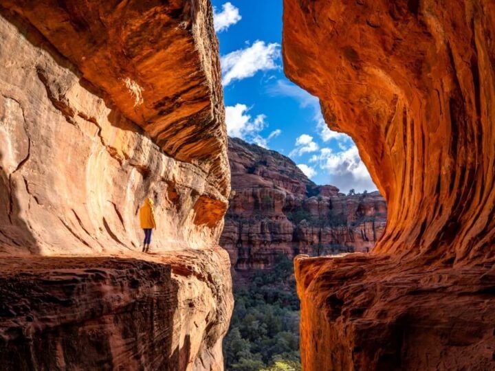 Hiker in yellow raincoat standing in the Subway Cave glowing orange one of the most popular caves in Sedona awesome photography and great hiking