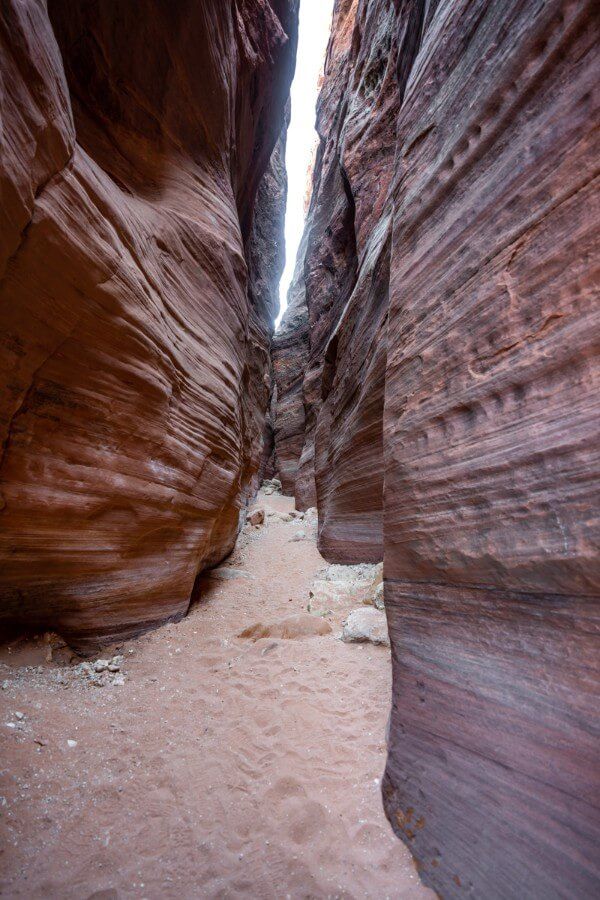 Slot Canyon with narrow walls and sandy trail thin crack of light appearing from above