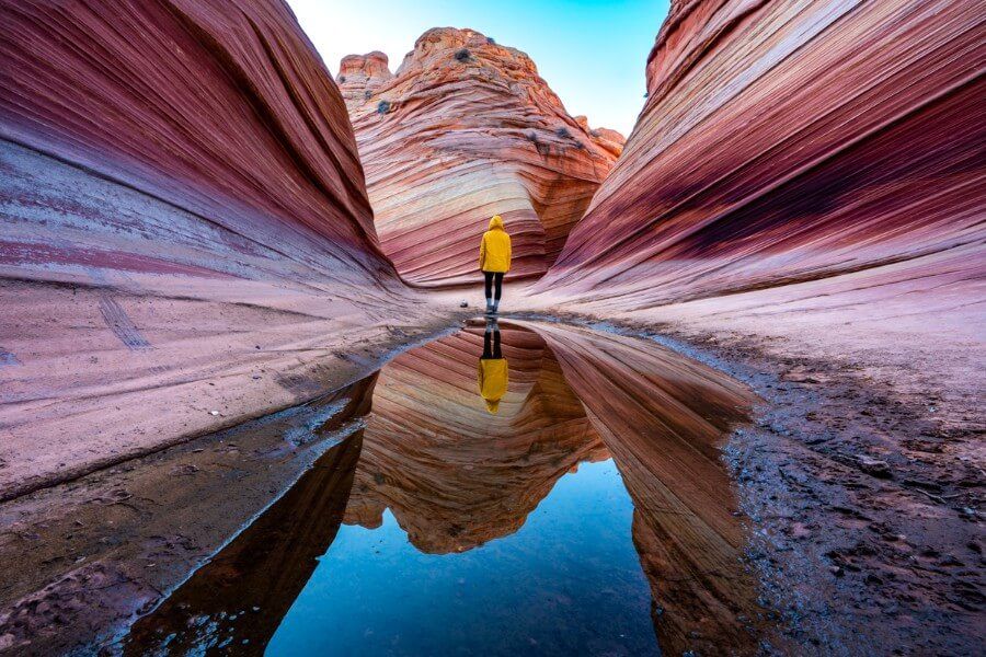 Hiker in yellow raincoat reflecting in pool of water at The Wave in Coyote Buttes North Arizona
