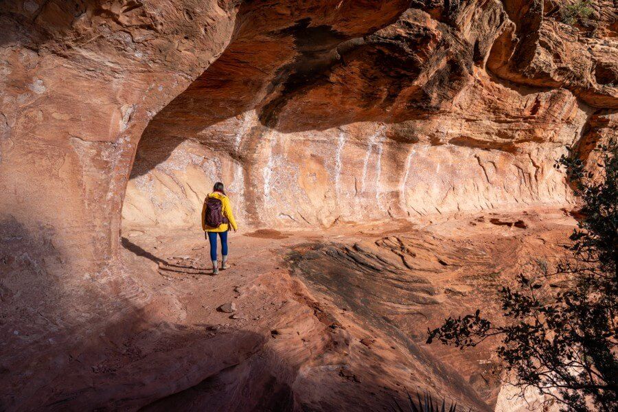 Hiker walking around a curving ledge on orange sandstone to access the subway cave in Sedona