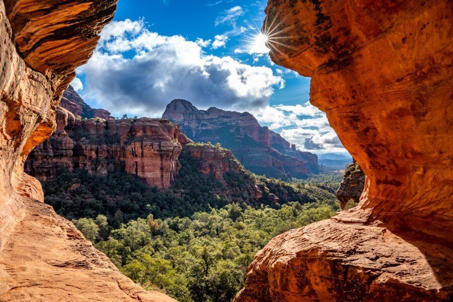 View over Sedona Arizona from inside the Subway Cave on Boynton Canyon trail hike red rocks green trees and starburst of the sun