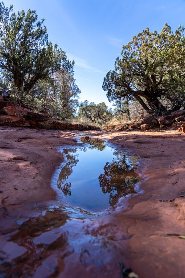 Puddles of water in a narrow wash on a bright blue day hiking Bell Rock Courthouse Butte Loop Trail in Sedona Arizona