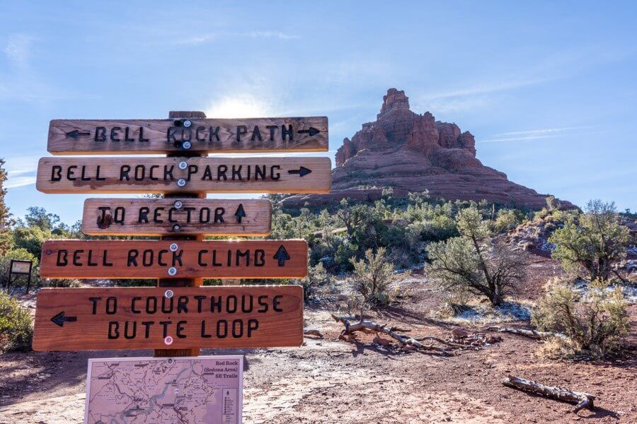 Lots of path directions markers on one big sign with rock formation in background