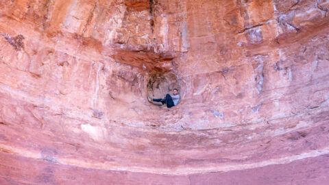 Hiker sat inside sphere shaped hole inside Birthing Cave off Long Canyon Trail in Sedona Arizona how to find and access the cave
