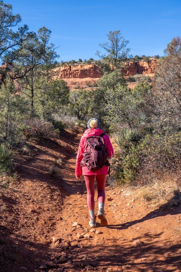 Hiker walking on a trail with coat and hat on a sunny day