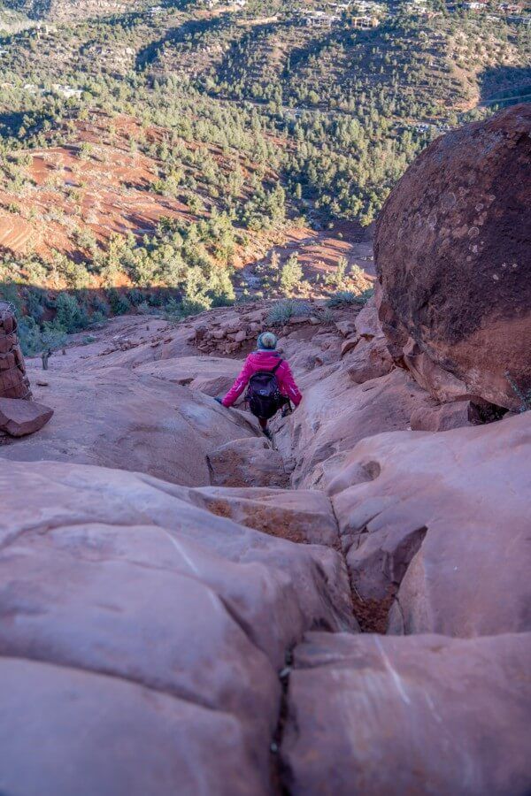 Sliding down a narrow slickrock section of the hike to Cathedral Rock Trail summit in Sedona AZ smooth rocks in shadow right after sunrise