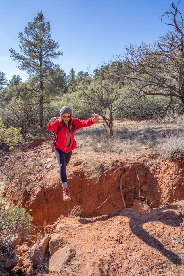 Hiker jumping over a wide ditch on a dusty dirt trail in arizona