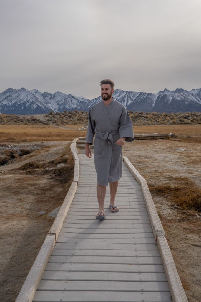 man walking down boardwalk with mountains in background