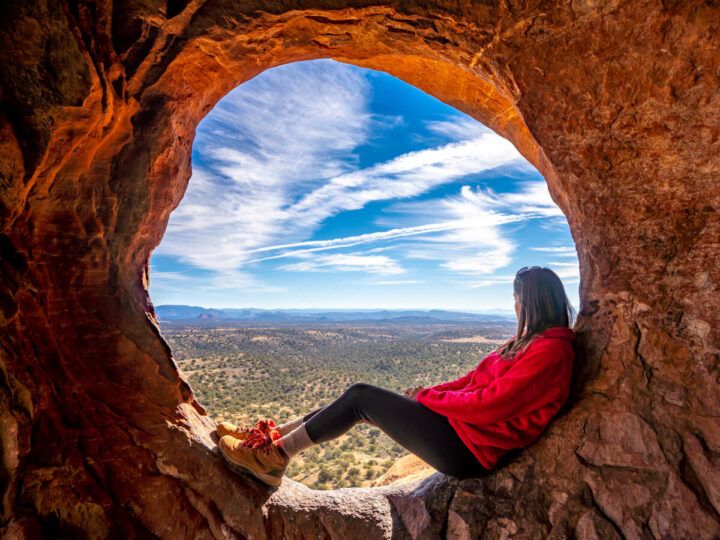 Hiker sat in a natural window inside Hideout Cave aka Shaman Cave after hiking Robbers Roost Trail in Sedona Arizona