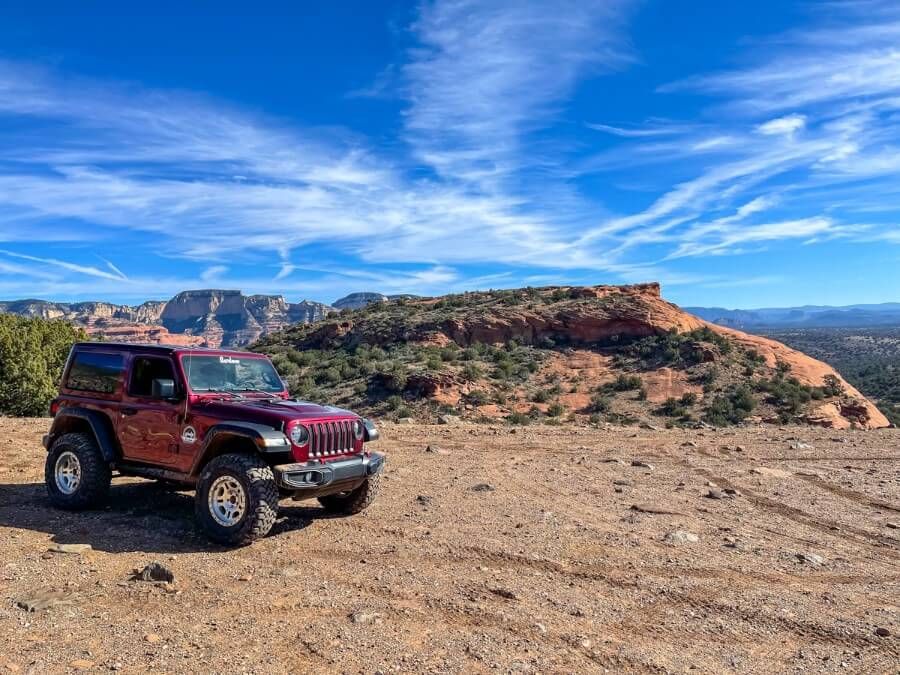 Jeep parked on a rocky flat area with red rocks behind on a sunny day in arizona