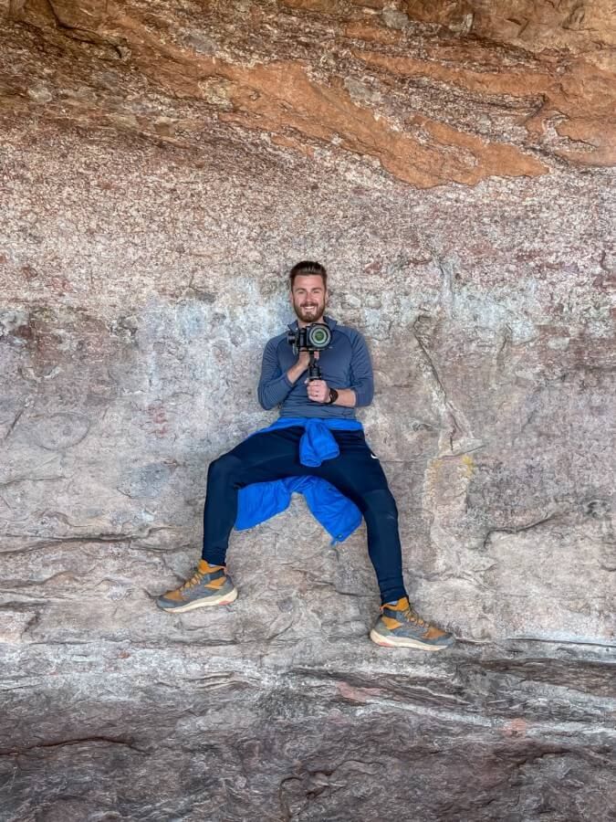 Hiker with camera and gimbal inside Hideout Cave on Robbers Roost Trail in Sedona on a sunny day in December