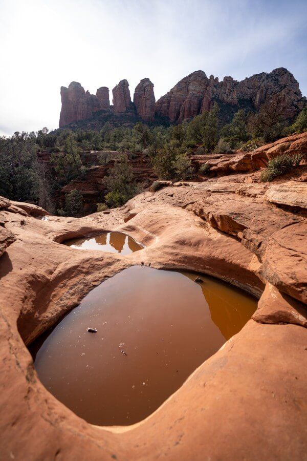 Pools of shallow water in red rocks with sandstone towers in the background