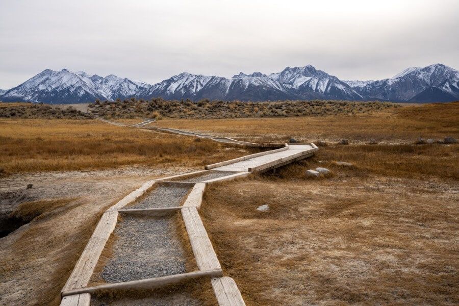 A long boardwalk with sierra nevada mountains in the distance at wild willys hot spring