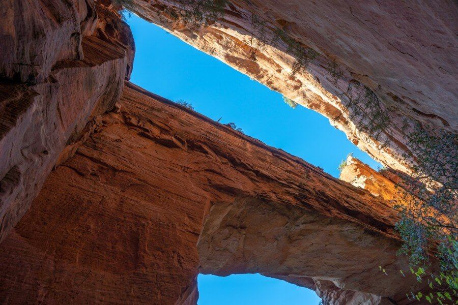 Looking directly up through a sandstone rock formation with clear blue sky behind