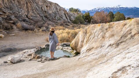 Women standing on the edge of travertine hot springs looking at mountains in the distance