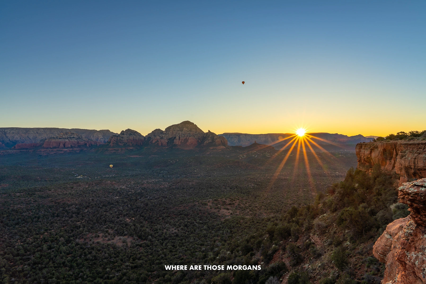 Photo of a sunrise with a starburst of the sun over a massive valley filled with vegetation and red rock formations from Doe Mountain in Sedona AZ at dawn