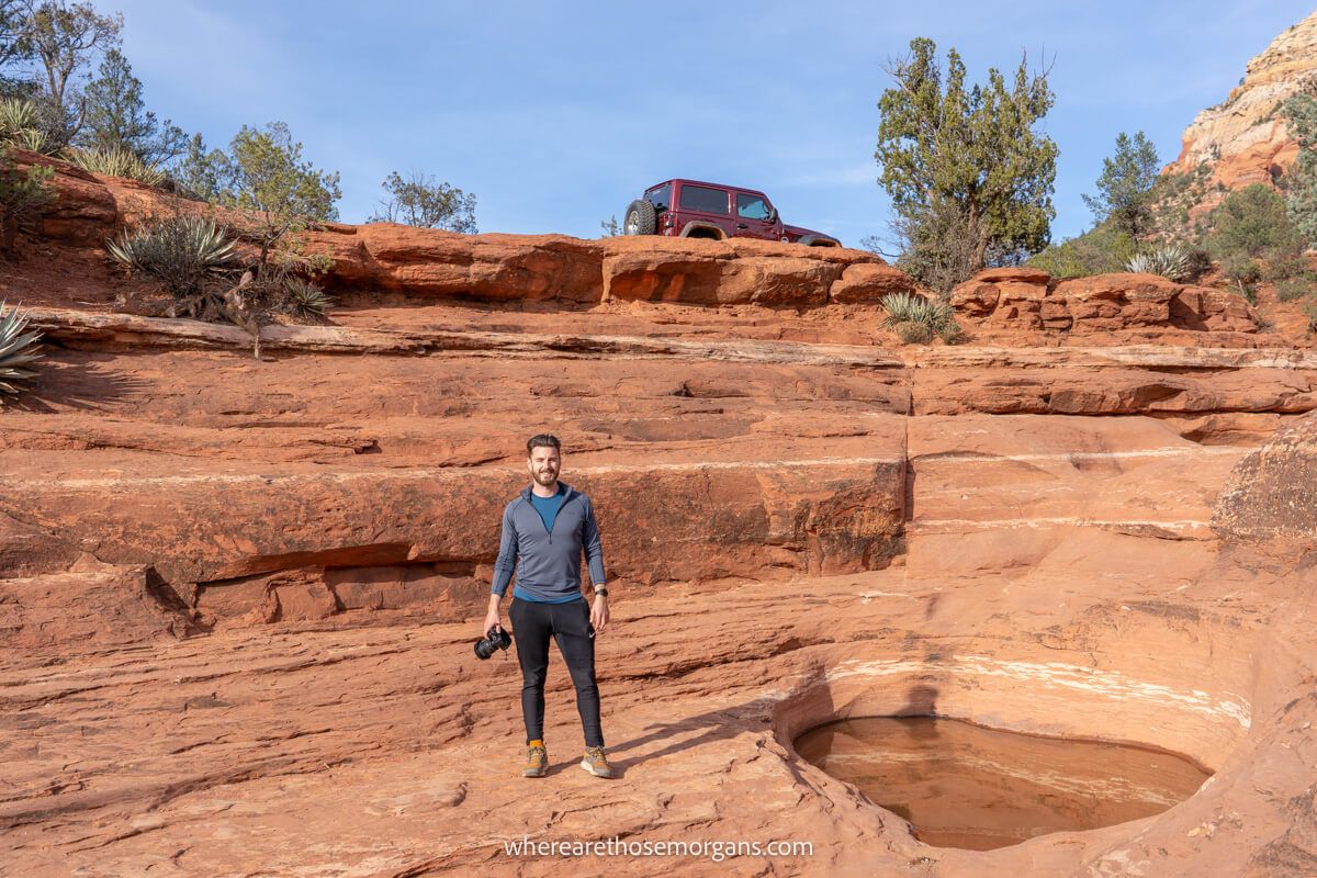 Hiker with camera next to a pool of water in a red rock landscape