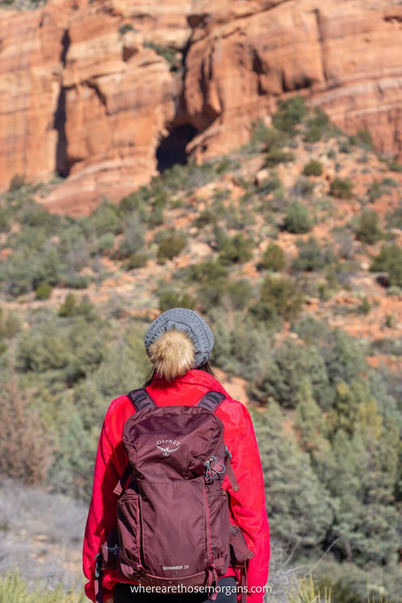 Hiker with hat on and Osprey backpack looking up at a red rock formation