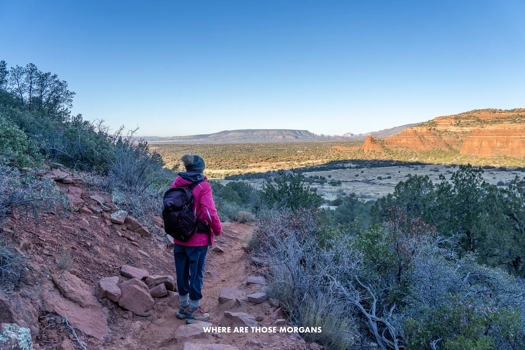 Photo of Kristen from Where Are Those Morgans hiking a red rock dirt trail at dawn in Arizona with lights and shadows