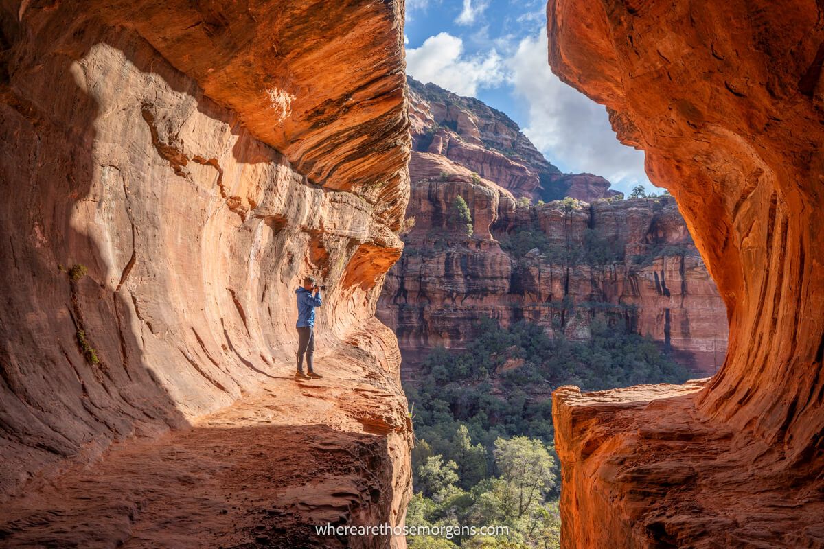 Hiker taking photos inside a tunnel-like red rock formation