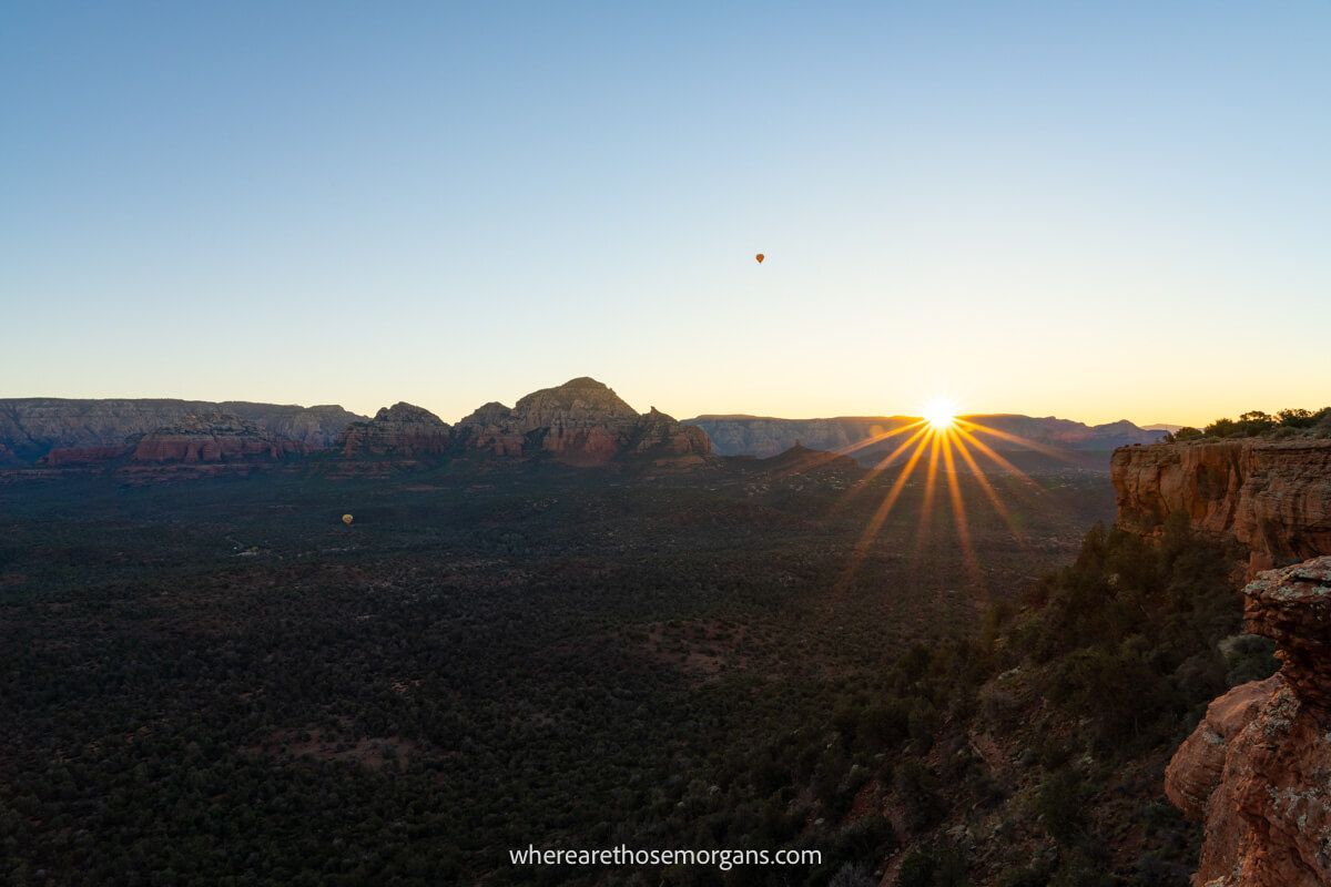 Photo of the sun rising over red rock formations in Sedona with a starburst effect on the sun as it bursts over the horizon