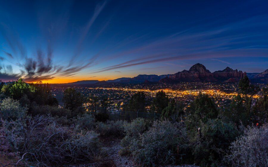Beautiful sunset photo of Sedona in Arizona taken from Airport Mesa vista overlook with vibrant colors in the sky and city lights shining below