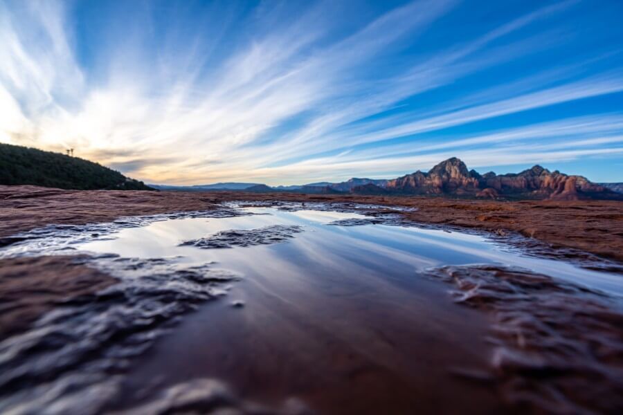 Wispy clouds reflecting in ice puddles in a red rock landscape