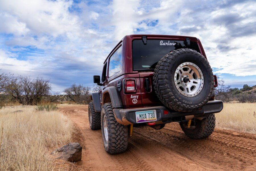 Maroon Rubicon parked on a dirt track close up from behind