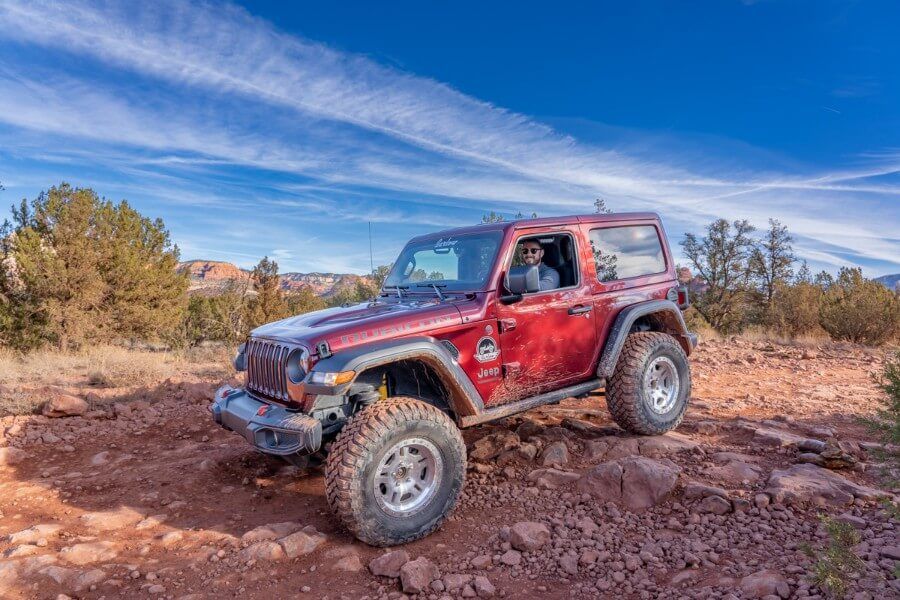 Maroon Jeep on rocks with smiling driver on a clear day with blue sky