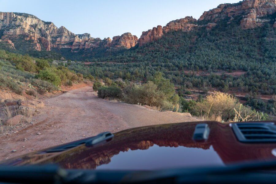 Photo taken through windshield of a dirt road cutting through red rock landscape