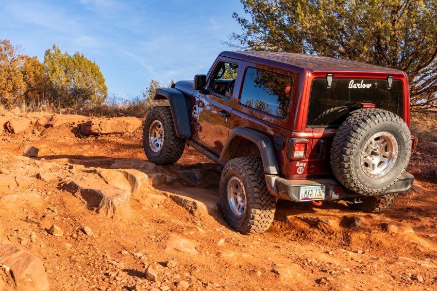 Driving a maroon Jeep up rocks on a dirt path during a sunny warm Winter day in Sedona in December