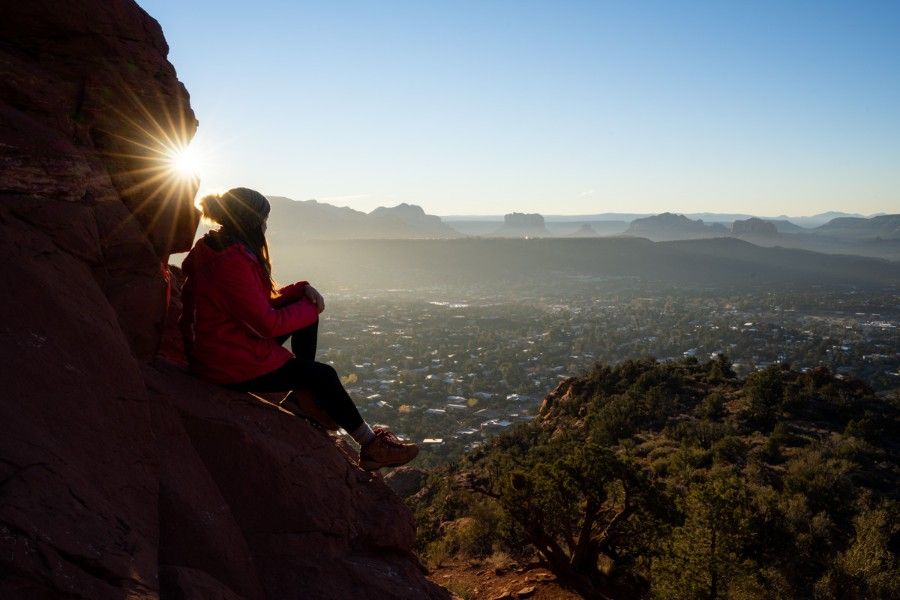 Hiker sat on red rocks watching sunrise over Sedona Arizona from the base of Chimney Rock spires