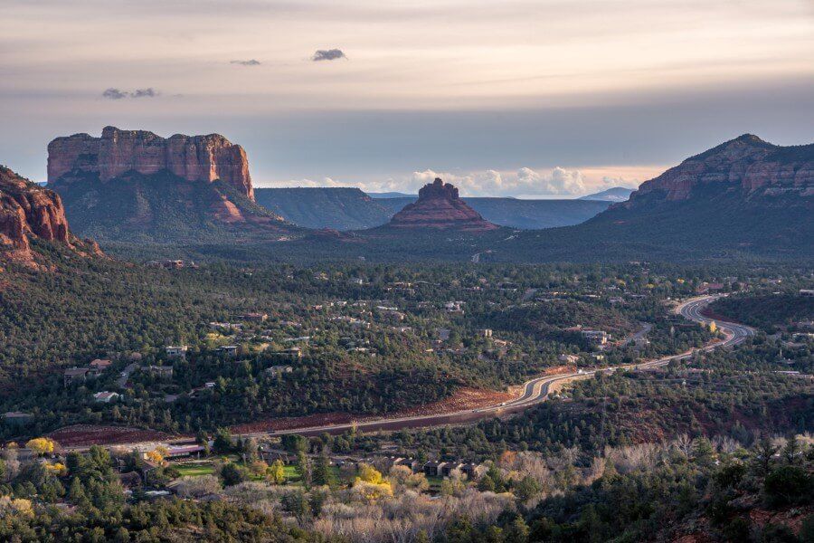 View over Bell Rock and Courthouse Butte with major road running through trees and red rocks in arizona