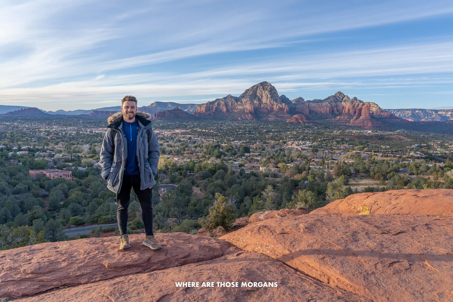 Photo of Mark Morgan wearing a heavy winter fur coat standing on red rocks with views over Sedona behind