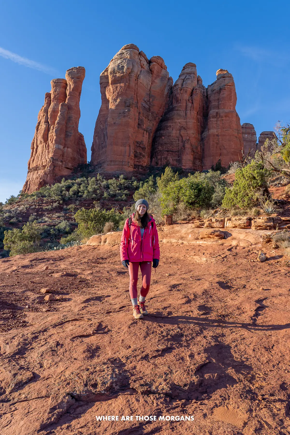 Photo of Kristen Morgan hiking down a steep red rock mountain with tall finger-shaped rock formations sticking up behind