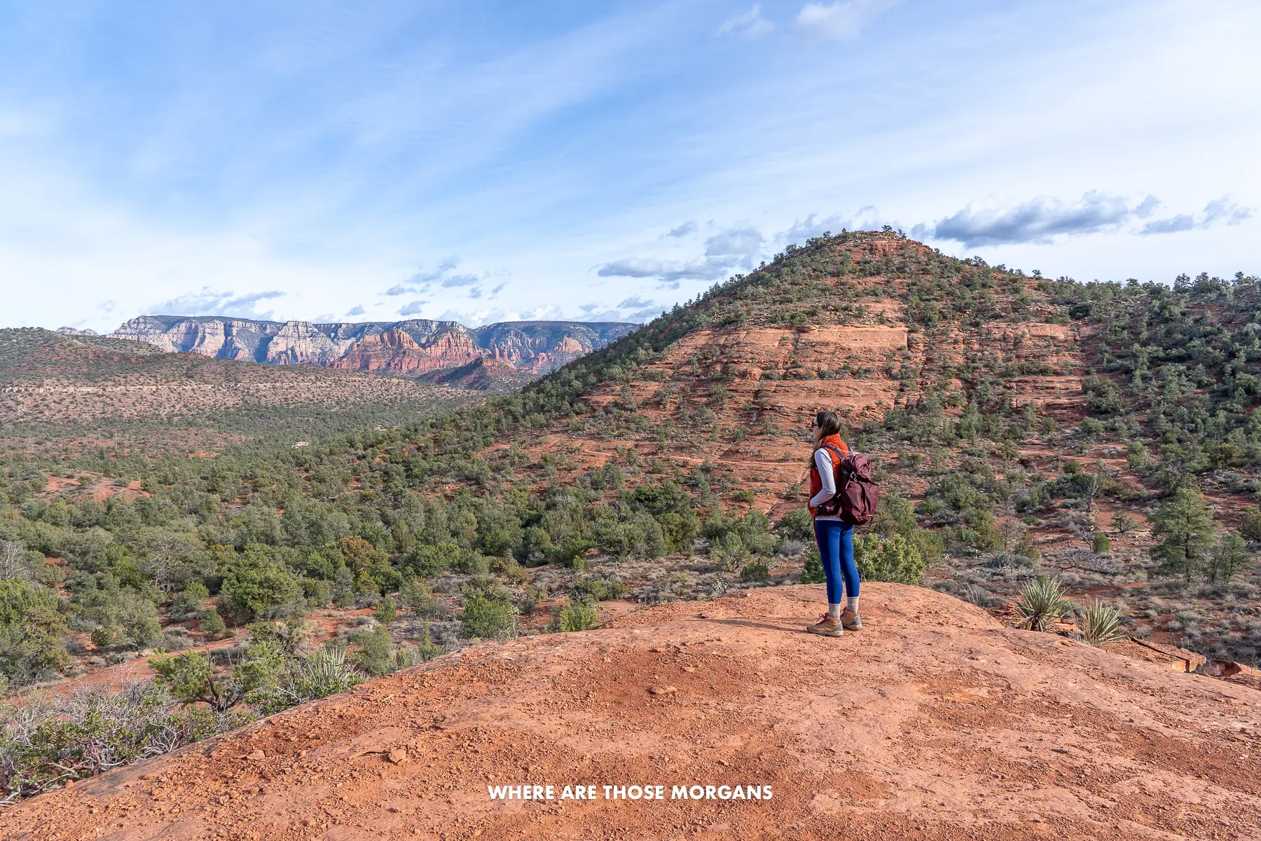 Photo of Kristen Morgan standing in hiking gear on a red rock trail looking at views over a desert landscape