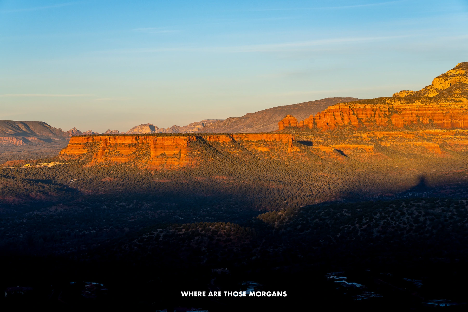 Photo of red rock mountains covered in orange sunrise light with deep dark shadows in the valley below
