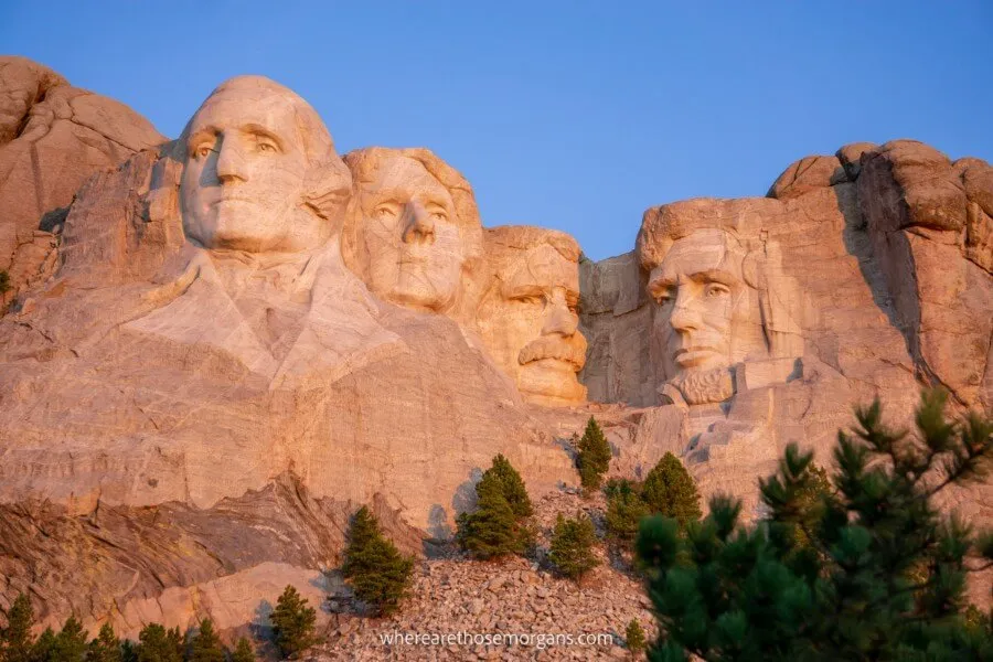 Mount Rushmore is one of the best places to visit in the USA lighting up pink and orange at sunrise in the Black Hills
