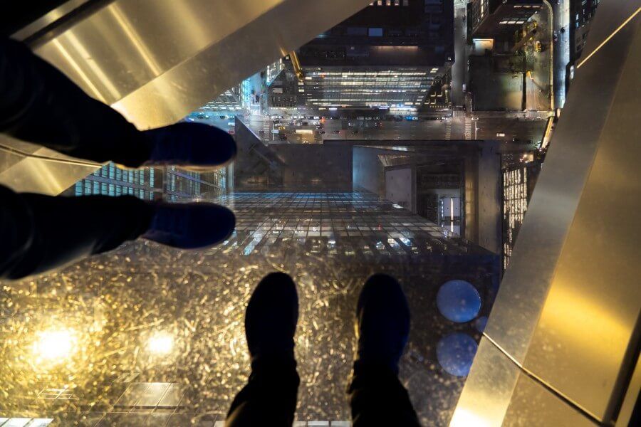Two set of feet standing over the glass panels on the Edge outdoor viewing platform