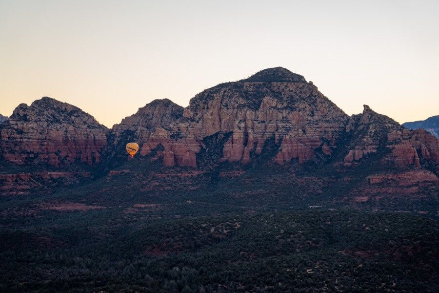 Hot air balloon taking off at sunrise with red rock background