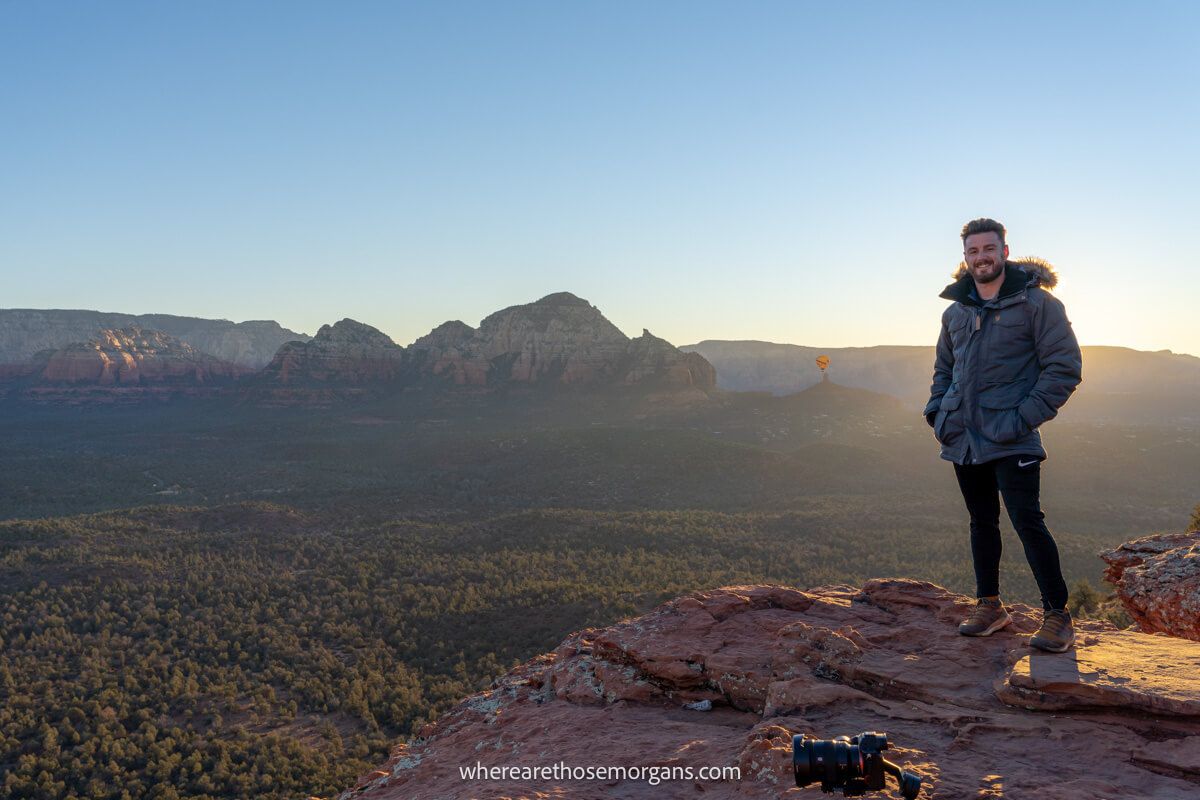 Hiker in winter coat stood on red rocks at sunrise with far reaching valley views behind