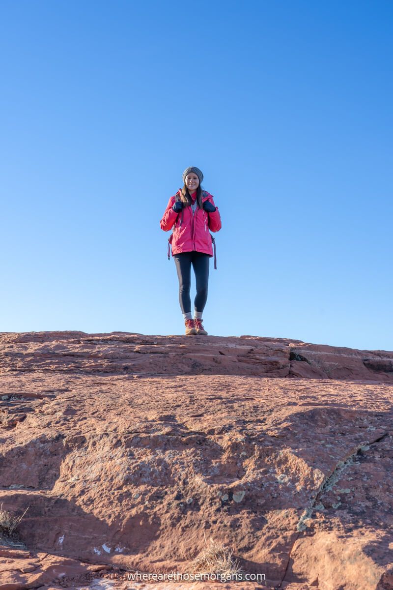 Hiker in pink winter coat stood on red rocks with a deep blue sky background