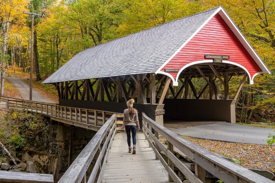 Woman walking towards a bright red covered bridge in New Hampshire