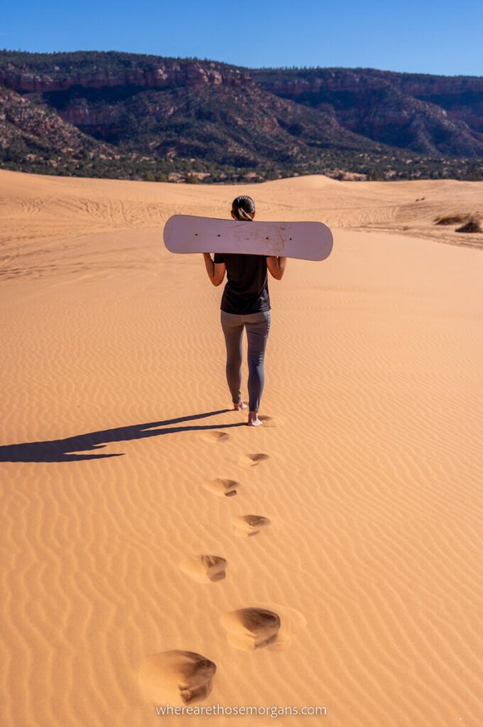 Sandboarder walking on Coral Pink Sand Dunes with footsteps one of the most fun things to do in Utah