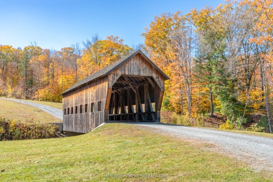 Stunning wooden covered bridge backed by colorful fall foliage leaves and blue sky
