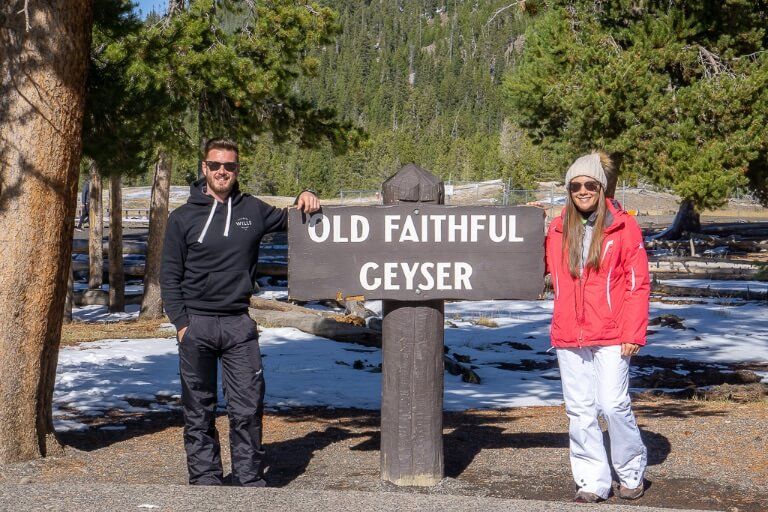 Man and woman standing with old faithful geyser sign