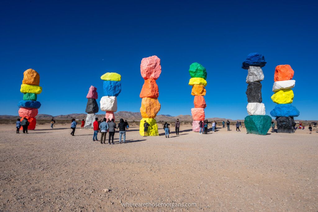 Seven Magic Mountains boulders painted vibrant colors and stacked with people taking photos around the towers and a deep blue sky
