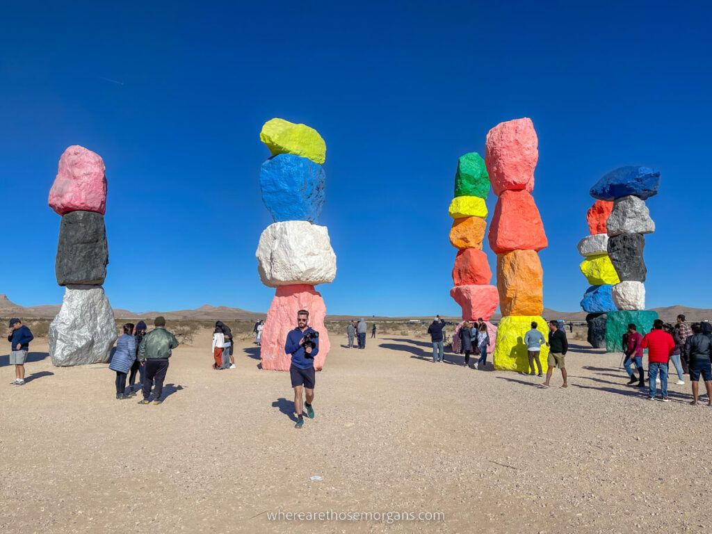Man with camera walking away from colorful stack of boulders on sand