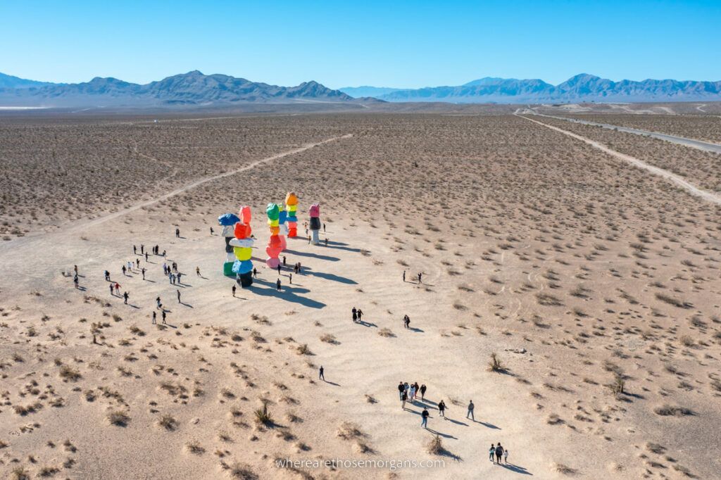 High up drone photo of Seven Magic Mountains art exhibit near Las Vegas with mountains in the background and I-15 running to the side
